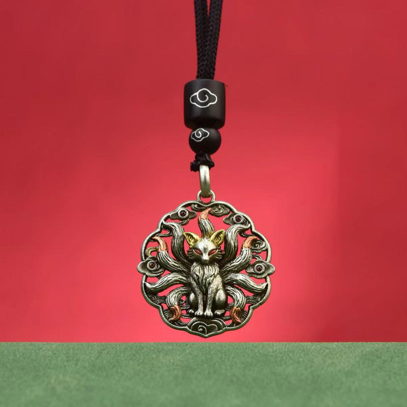Nine-tailed fox pendant on braided black cord with cloud-pattern beads, photographed against a traditional red and green backdrop