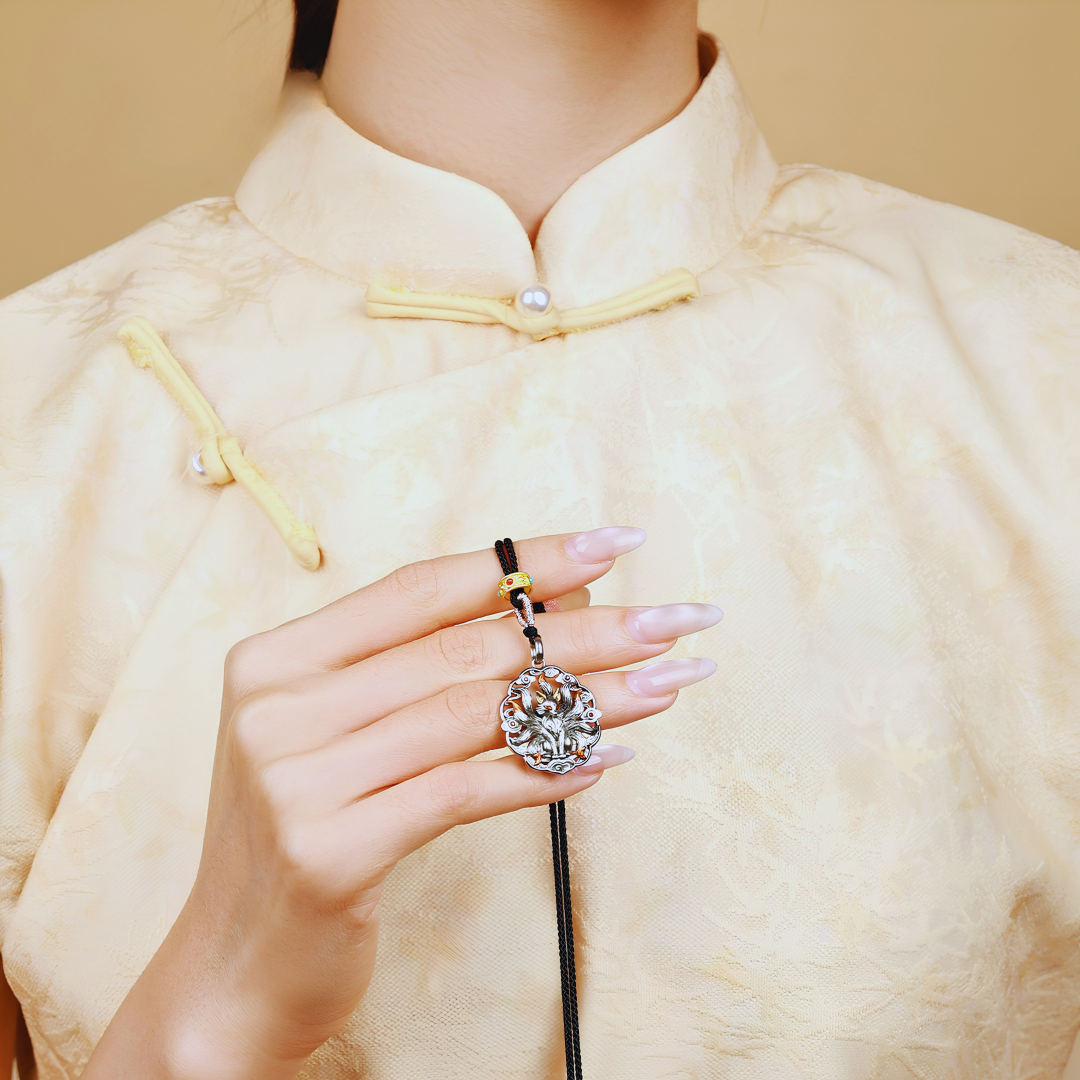 Nine-tailed fox pendant necklace worn by a model in a cream traditional Chinese garment, showing actual wearable size and styling with a black braided cord