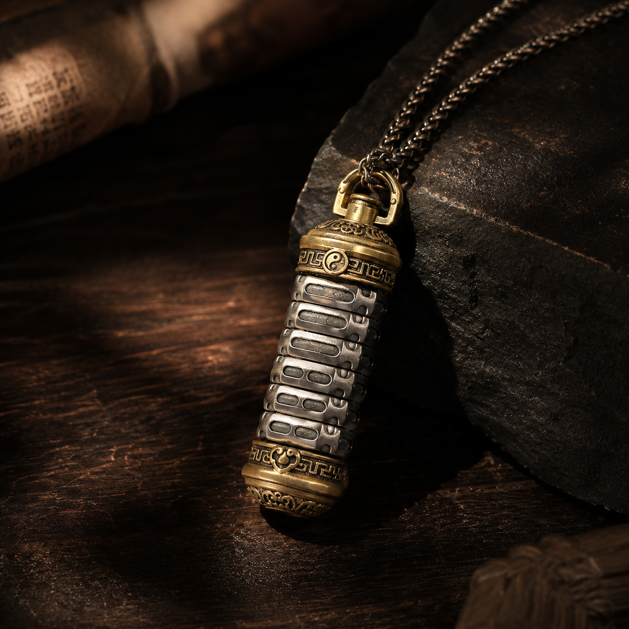 Revolving Mantra copper pendant displayed on dark slate rock with antique scroll and wooden props, showing two-tone brass and silver finish with intricate cloud and meander carvings under dramatic warm lighting